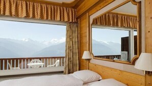 Een hotelkamer met twee bedden, een groot raam met uitzicht op bergen, een houten hoofdbord en een spiegel.