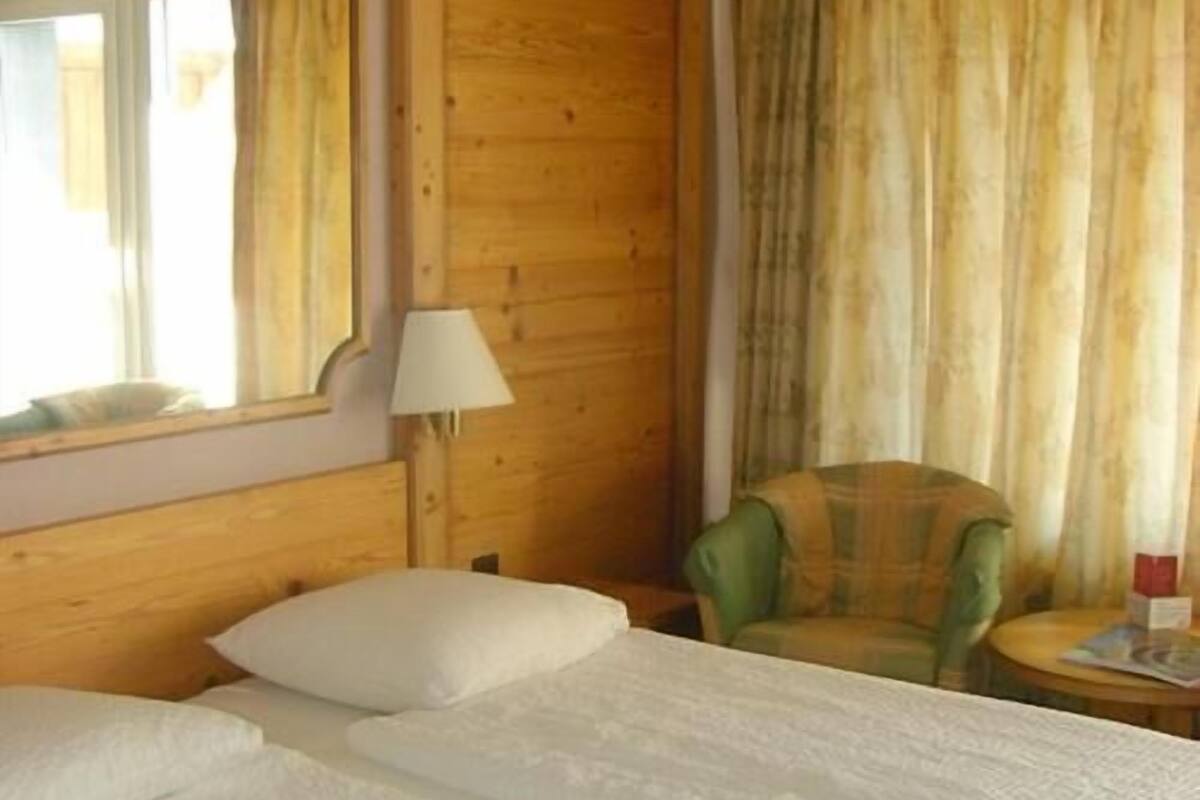 Ein Zimmer mit Holzboden, einem Bett, einem Sessel und einer Lampe.