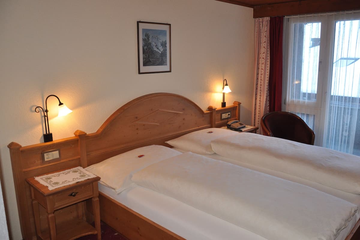 A double bed with wooden headboard and nightstands, two bedside lamps, a framed picture on the wall, and a window with curtains.