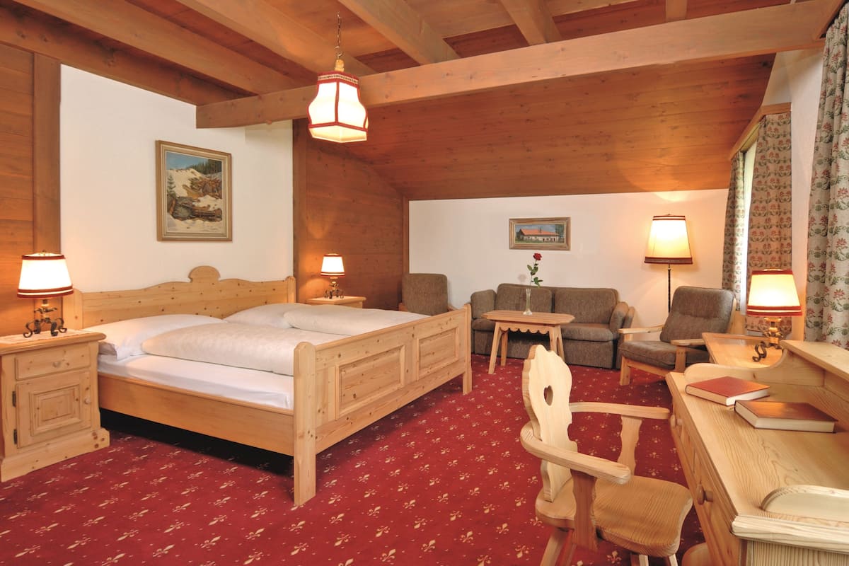A wooden bedroom with a bed, a desk, a chair, a sofa, and two lamps.