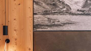 A bedroom with a wooden headboard, a bedside table with a lamp, a red pillow, and a large black-and-white mountain landscape painting on the wall.