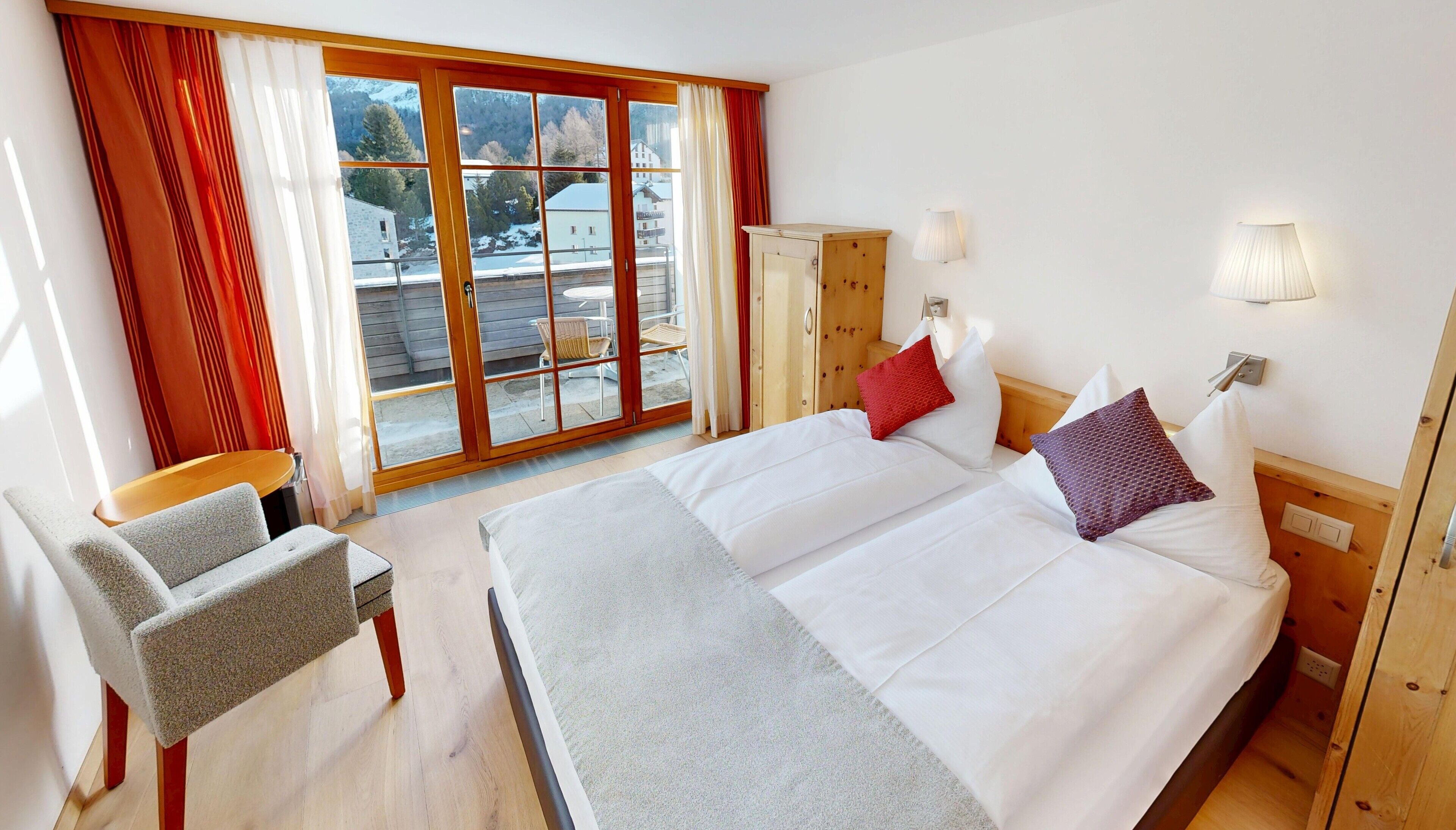 A hotel room with a large bed, a chair, a wardrobe, and a view of the outside.