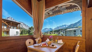 Un comedor de madera con una mesa dispuesta para el desayuno, vistas a montañas y una pérgola de madera.