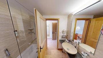 A modern bathroom with a glass-enclosed shower, a vanity with a sink and mirror, and a wooden door leading to another room.