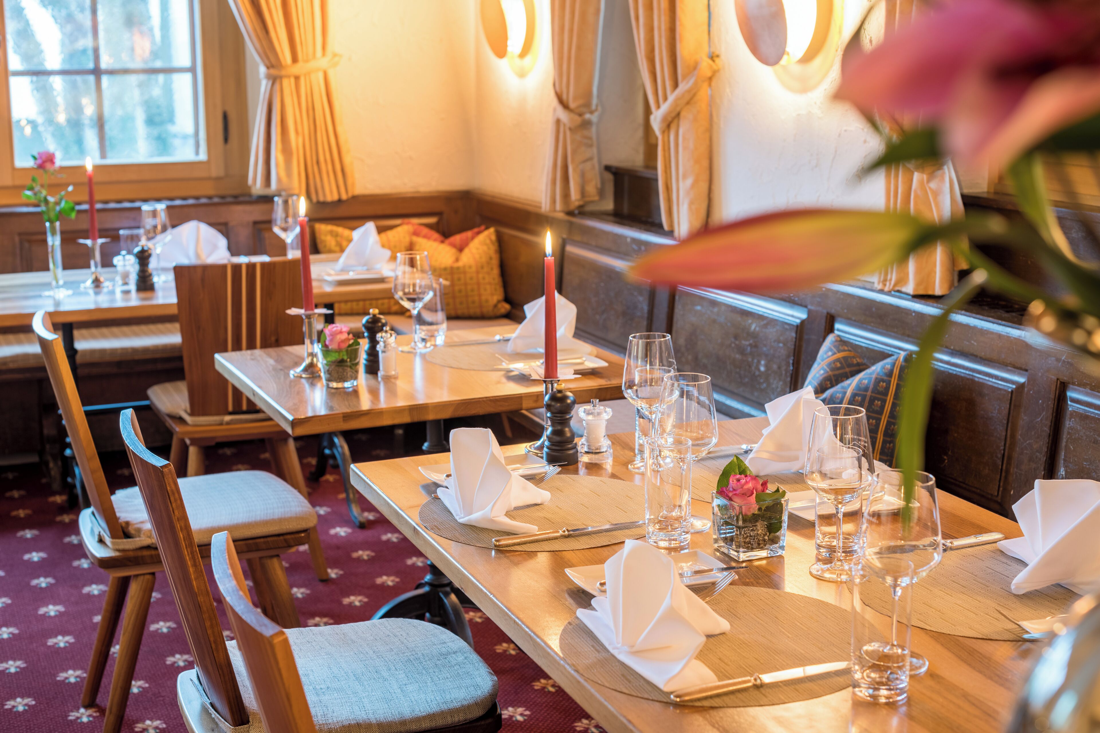 Un restaurante con mesas de madera dispuestas para comer, velas y centros de mesa con flores.