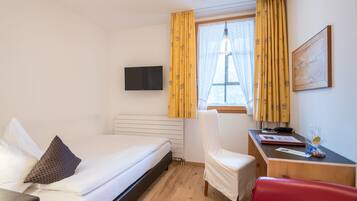 Habitación de hotel con cama, escritorio, silla, televisor y ventana con cortinas.