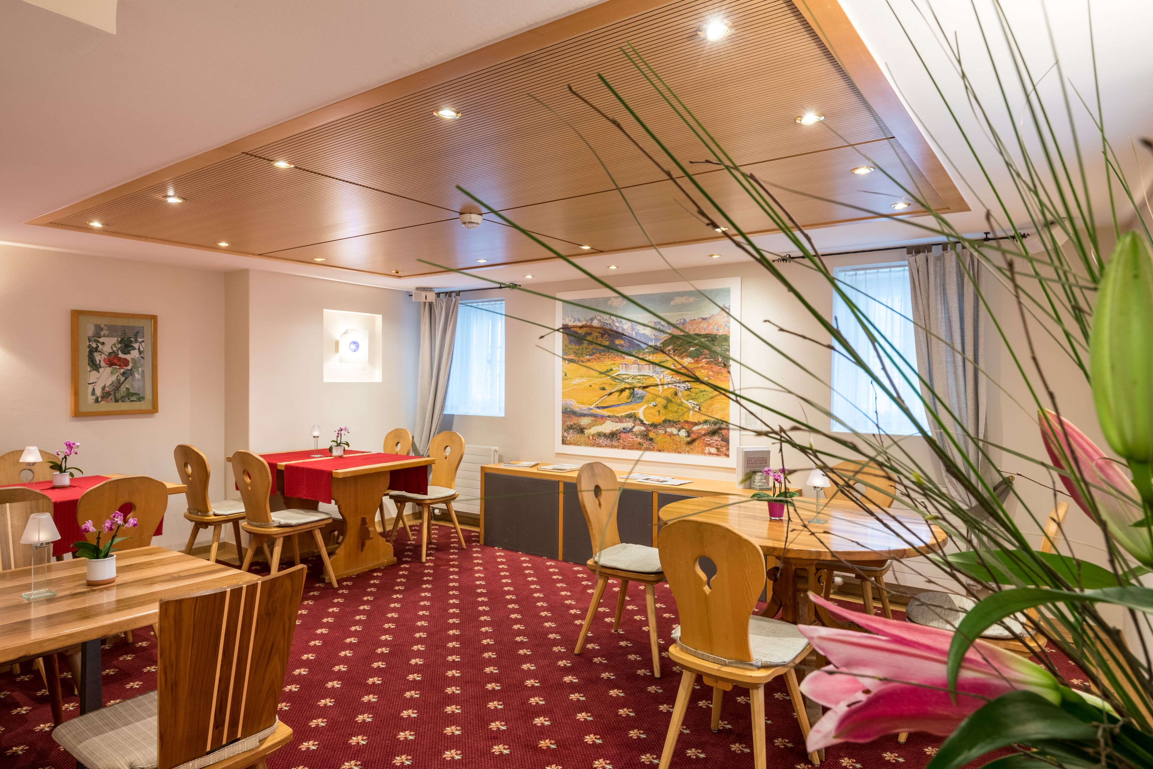 Un espace repas avec des tables et des chaises en bois, une moquette rouge et un tableau accroché au mur.