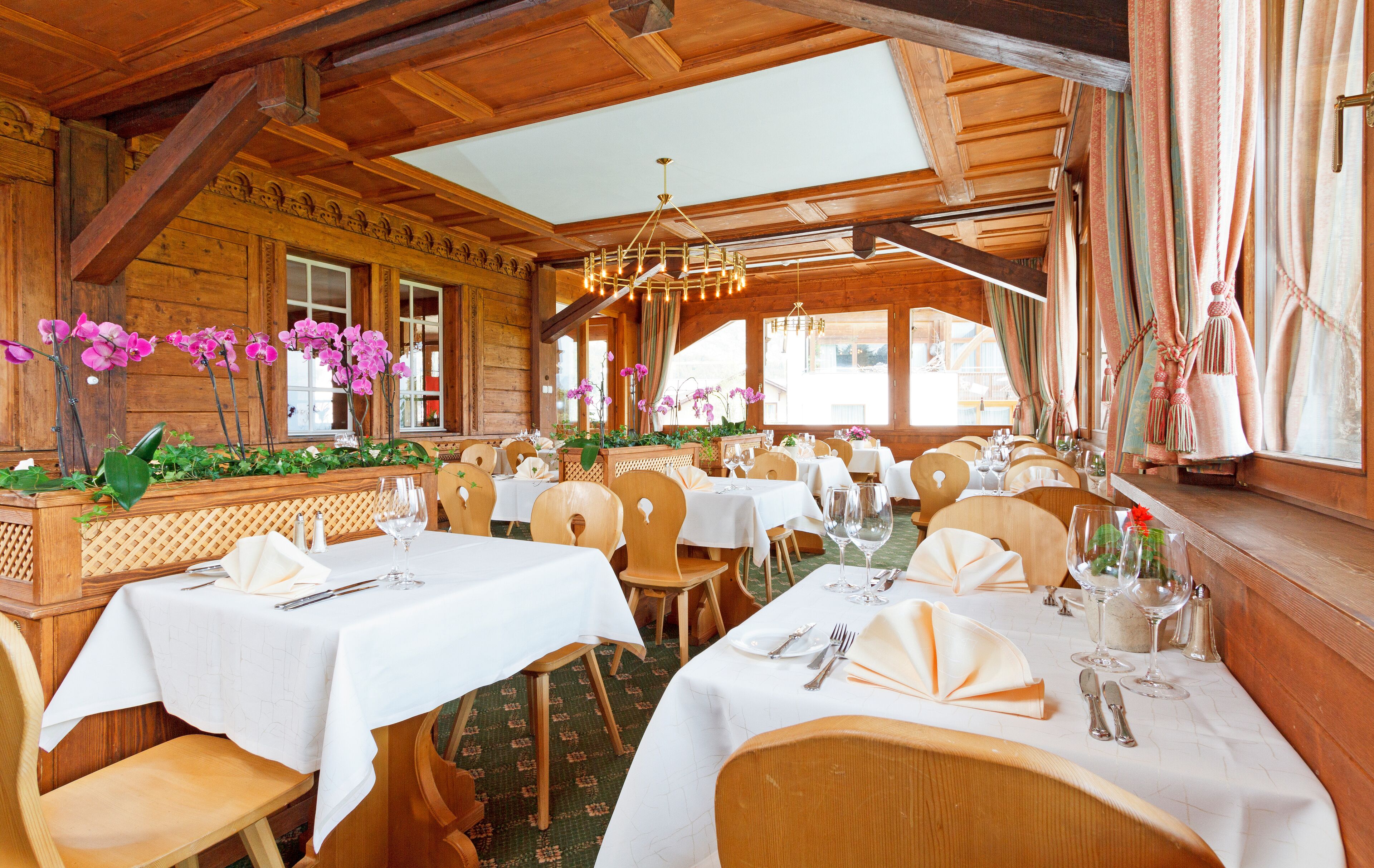 Un ristorante con interni in legno, tovaglie bianche e orchidee viola.