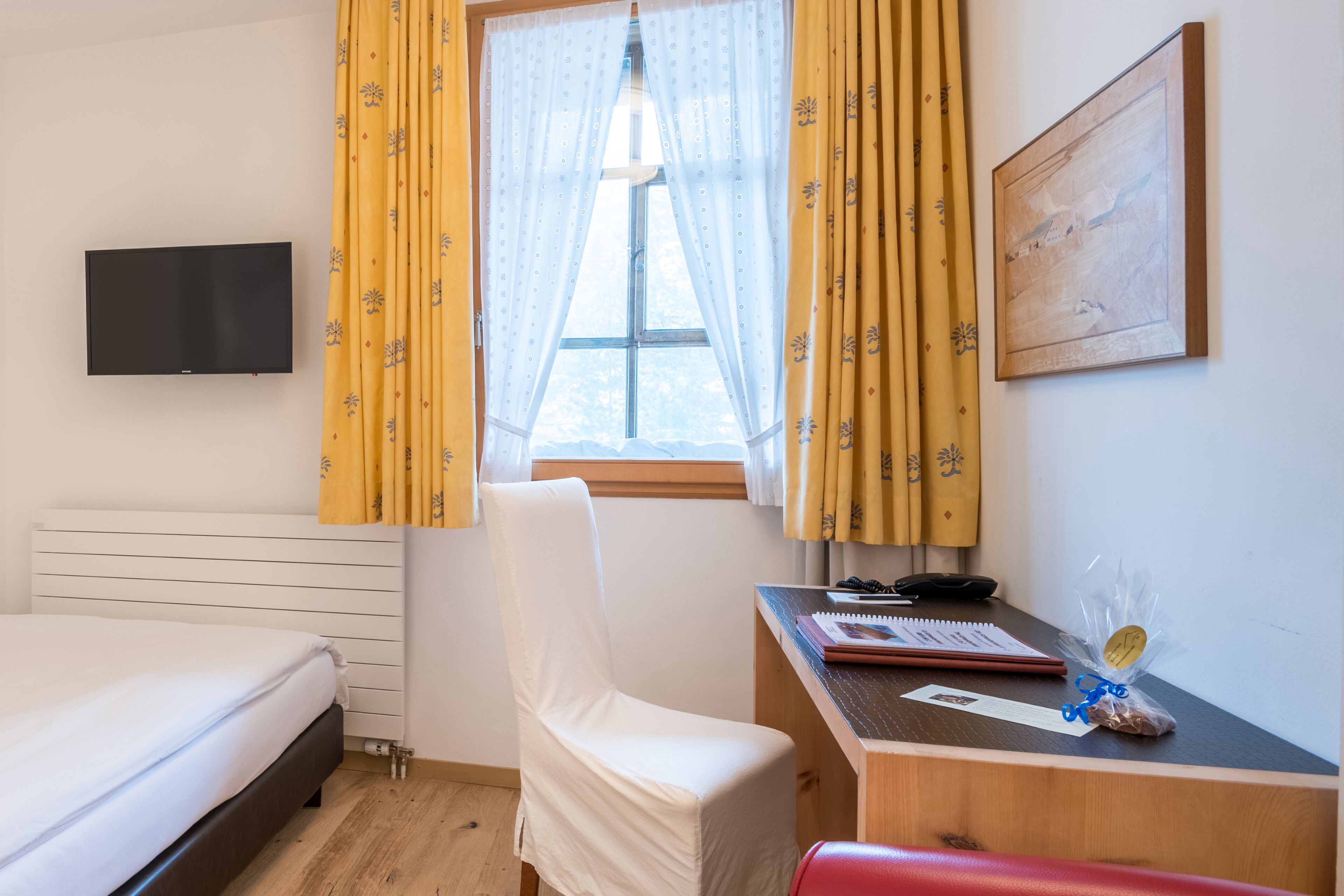 Une chambre d’hôtel avec un lit, un bureau, une chaise, une télévision et une fenêtre avec des rideaux.