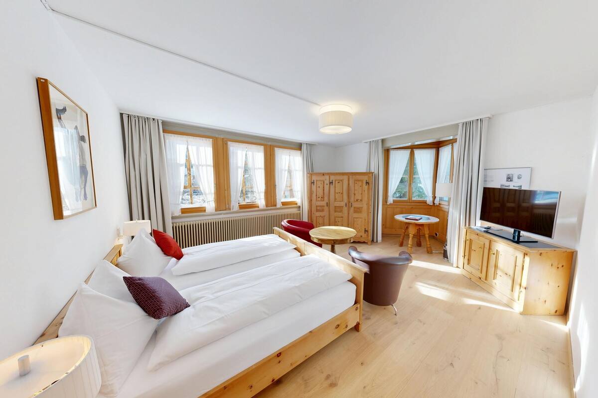 Ein Hotelzimmer mit einem großen Bett, einem Fernseher, einer Holzkommode, einem kleinen Tisch und einem roten Sessel.