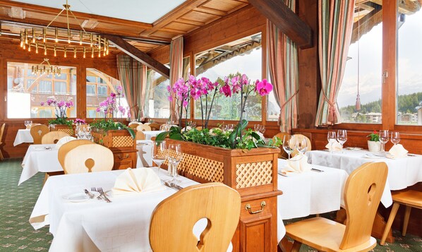 A restaurant with wooden interiors, white tablecloths, and purple orchids. - Schweizerhaus Swiss Quality Hotel (Bregaglia)