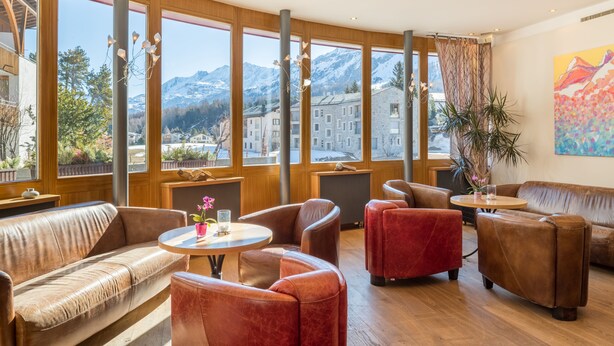 Un interior moderno con sofás de cuero, una mesa redonda y ventanas amplias que ofrecen vista a las montañas.