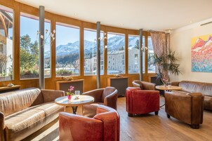 Un interior moderno con sofás de cuero, una mesa redonda y ventanas amplias que ofrecen vista a las montañas.
