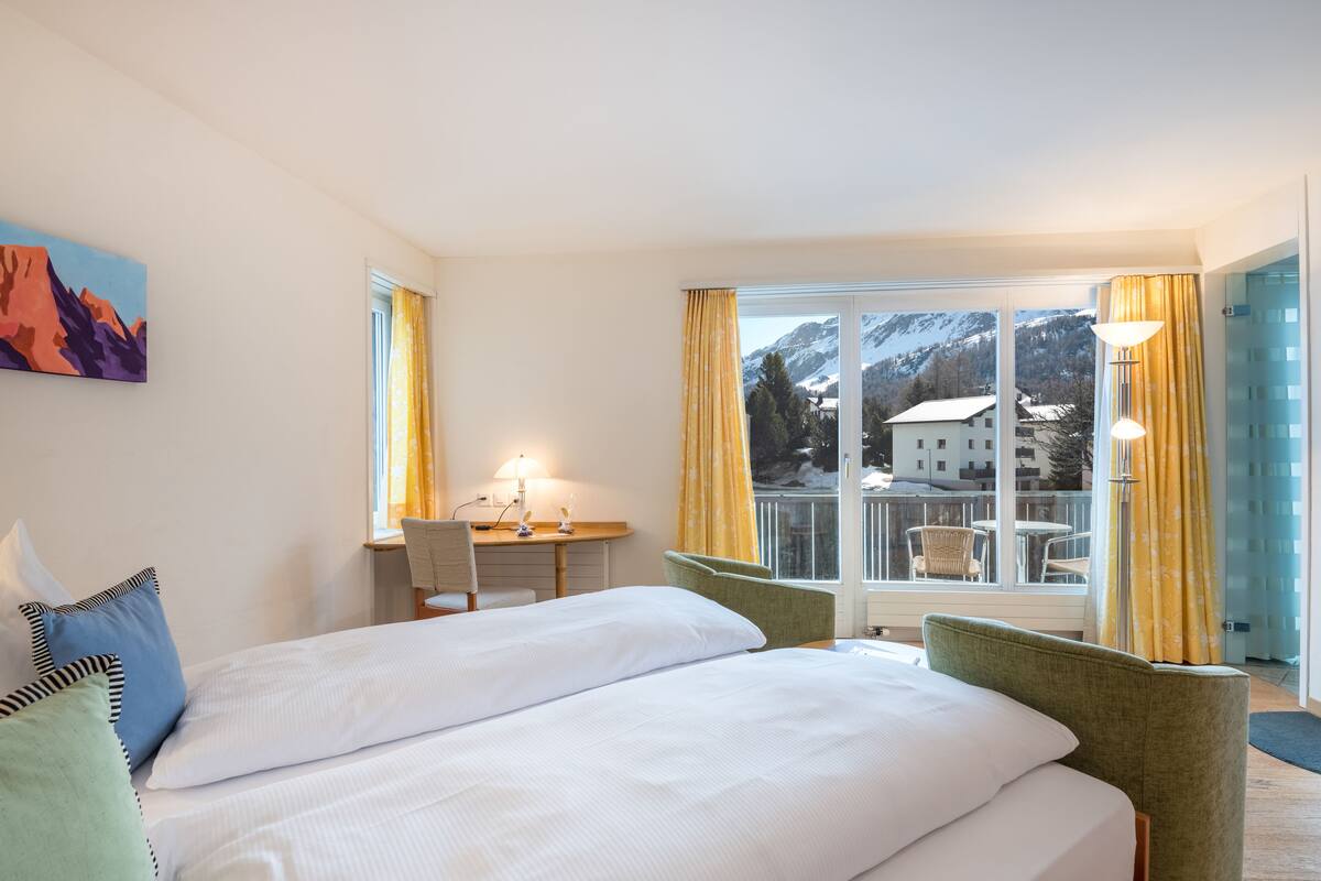 Ein Hotelzimmer mit einem großen Bett, einem Schreibtisch und Blick auf Berge durch das Fenster.