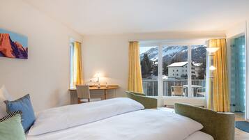 Ein Hotelzimmer mit einem großen Bett, einem Schreibtisch und Blick auf Berge durch das Fenster.
