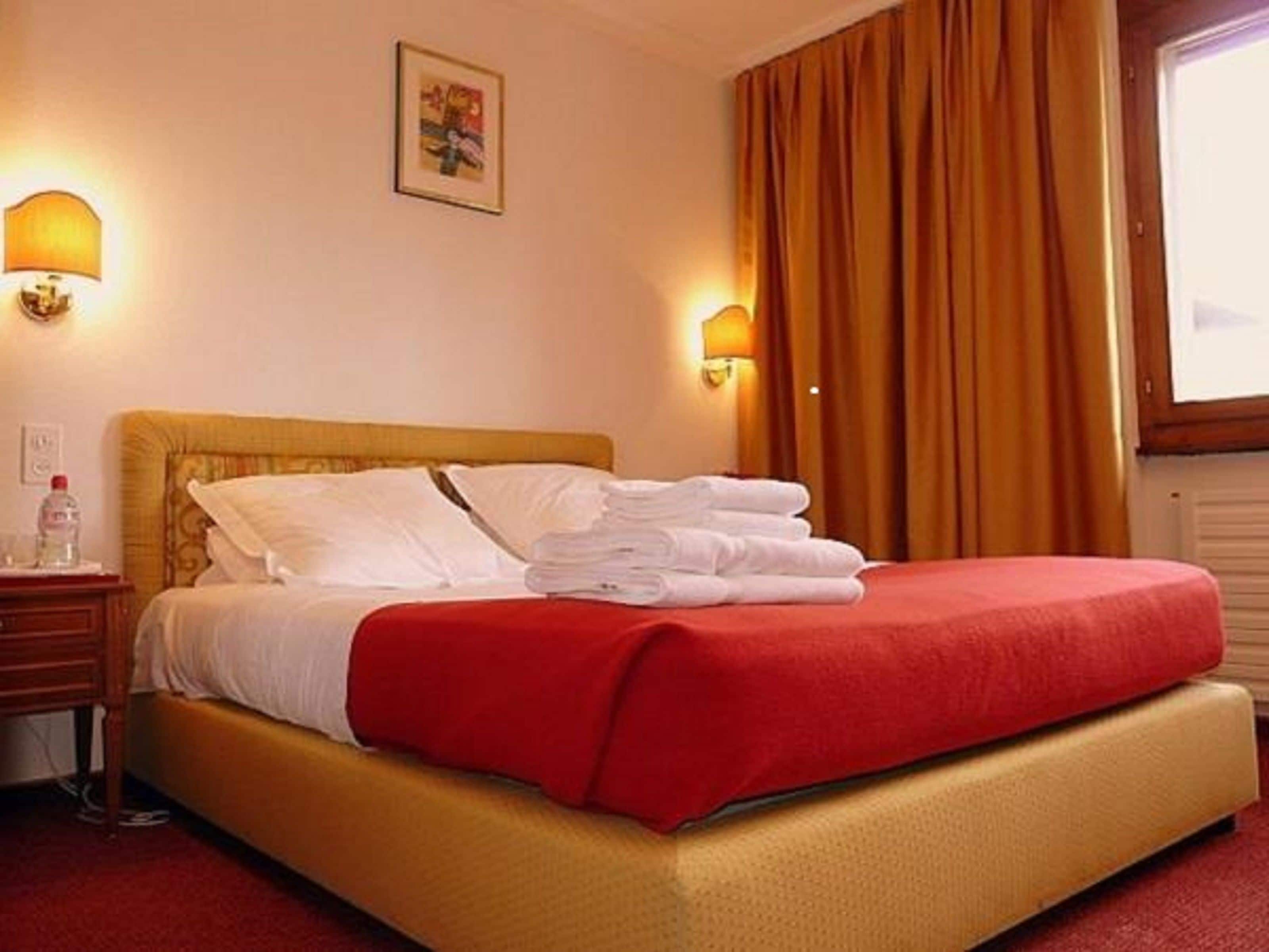 Une chambre d’hôtel avec un lit, une table de chevet, une lampe et une fenêtre avec des rideaux.