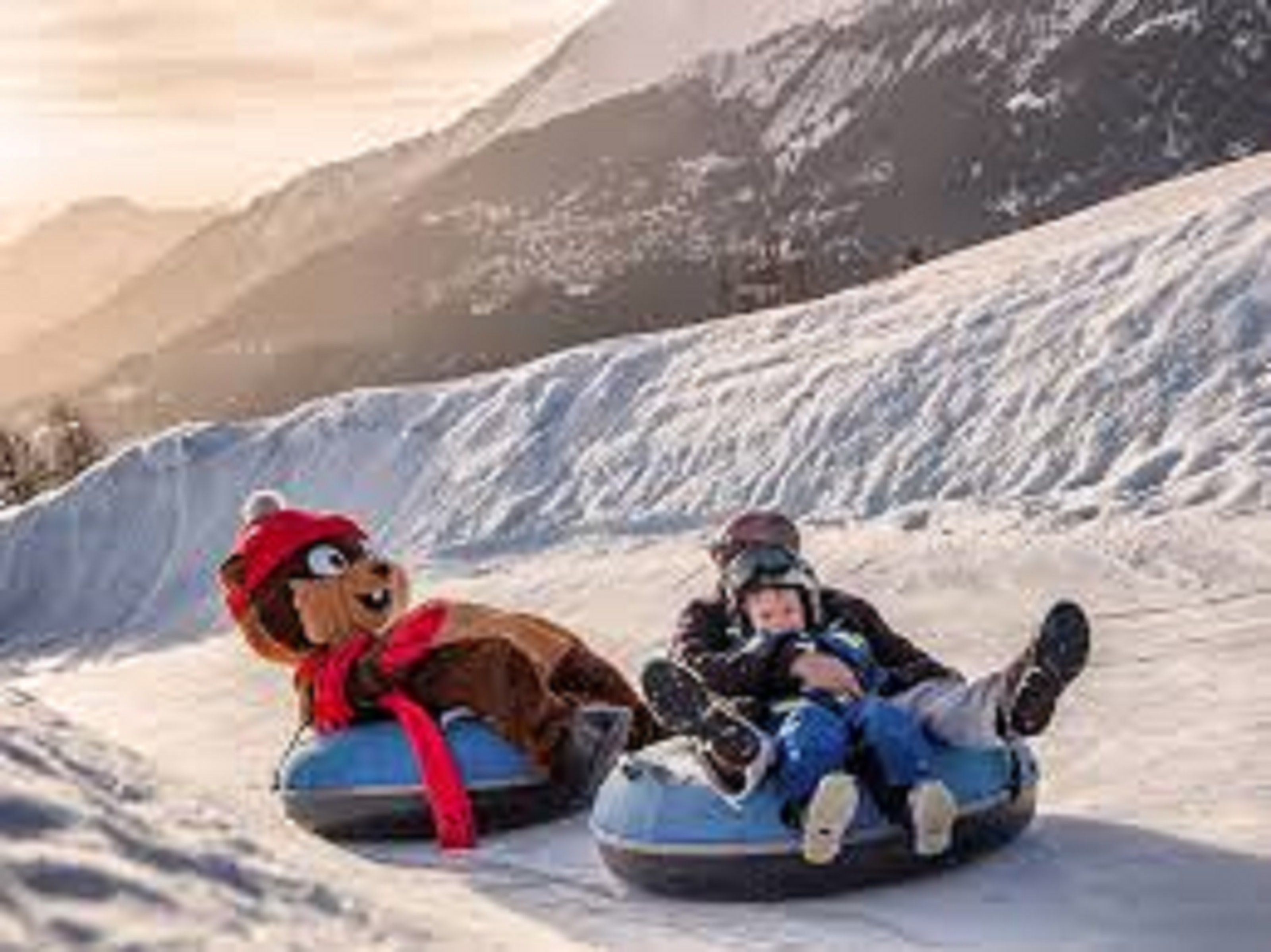 Dos personas en neumáticos para nieve con un personaje animado en un paisaje montañoso nevado.