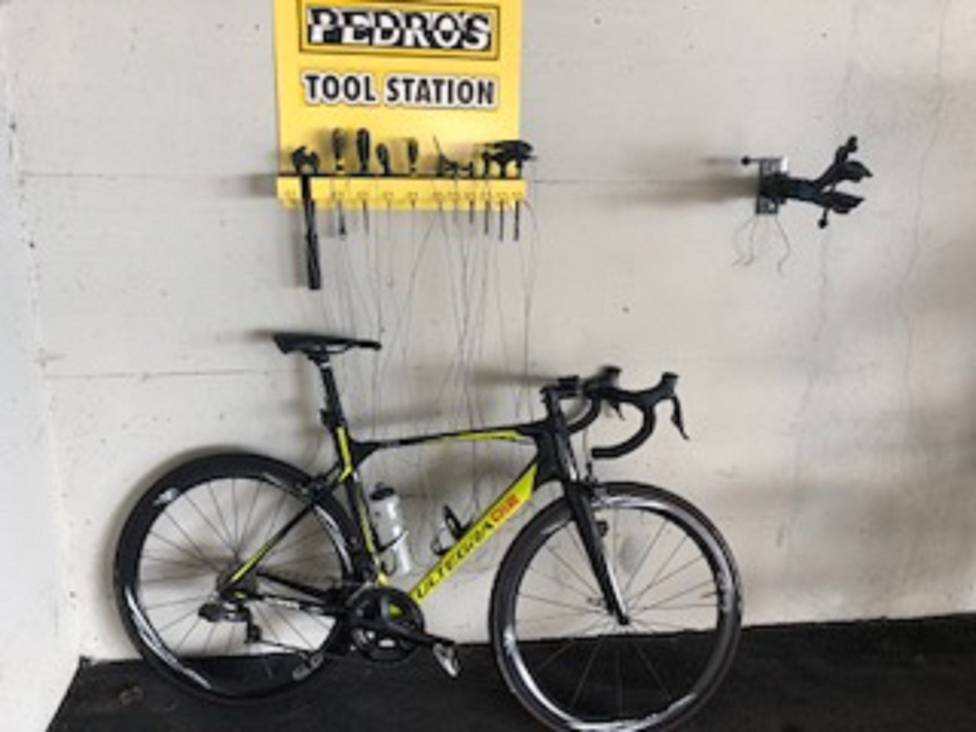 A bicycle leaning against a wall with a yellow sign above it that reads "PEDRO'S TOOL STATION".