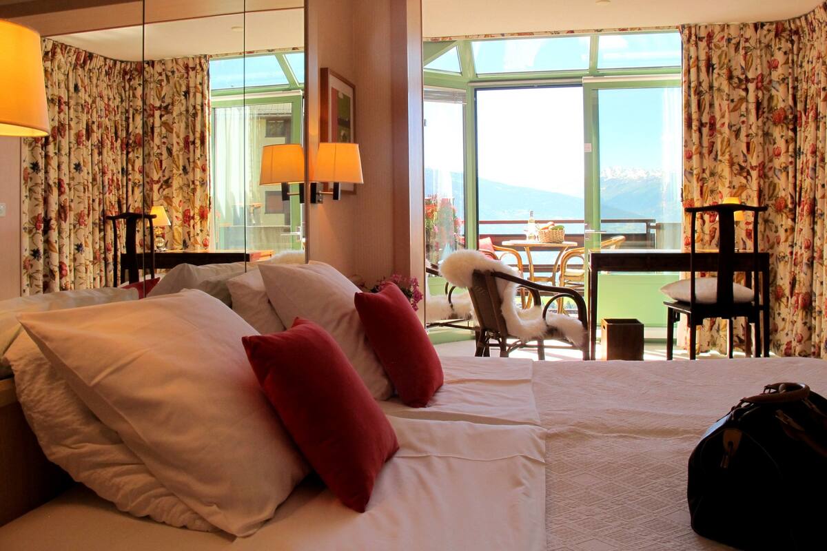 A hotel room with a bed, two chairs, a table, and a view of the outdoors.