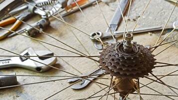 A bicycle wheel with a spoked hub and spokes, surrounded by tools like pliers and a wrench on a wooden surface.