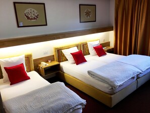 A hotel room with two beds, each with white linens and red pillows, a wooden headboard, a nightstand with a phone and a small table, and framed artwork on the wall. - Hôtel Résidence de la Forêt (Crans-Montana)