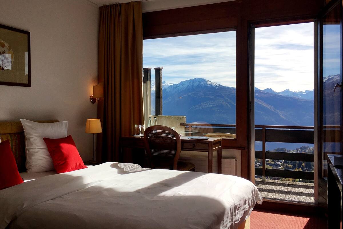 A hotel room with a bed, a desk, and a view of mountains.
