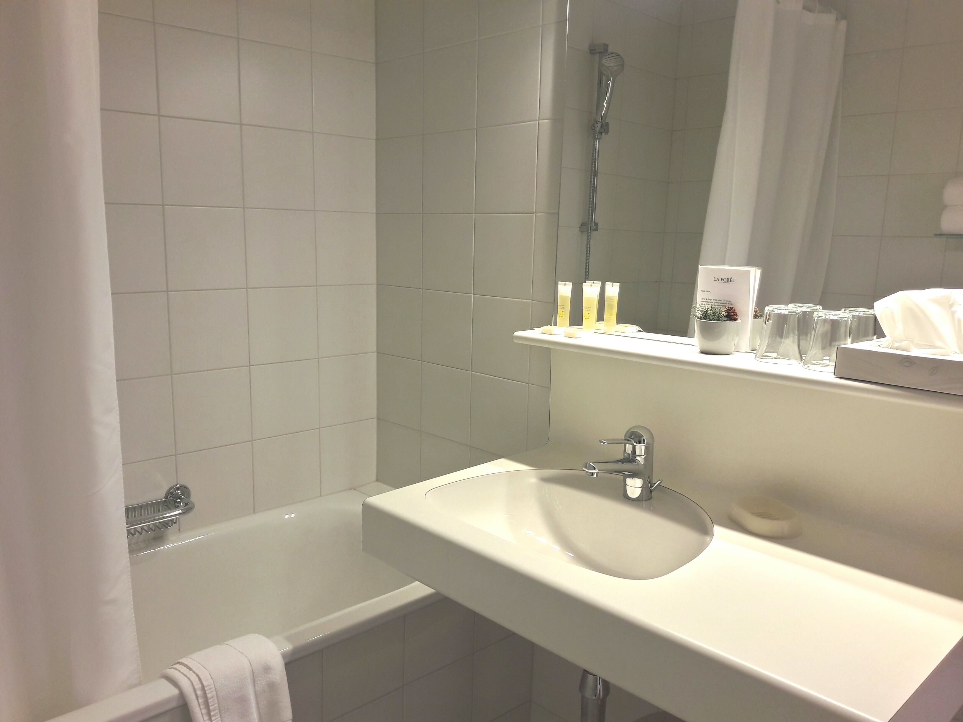 Un baño con una bañera blanca, un lavamanos y una ducha. Hay artículos de aseo en el lavamanos y una toalla colgada en la pared.