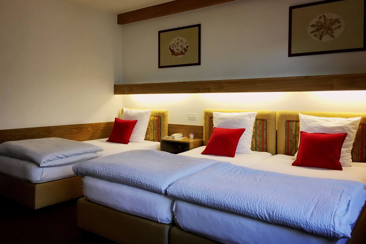 A hotel room with two beds, each with a headboard, white linens, and red pillows. There are framed pictures on the wall above the beds.