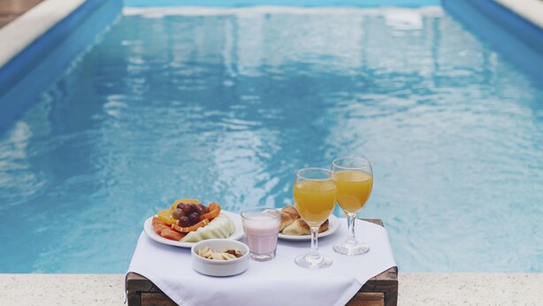 A poolside table with a plate of fruit, two glasses of orange juice, and a small bowl of nuts. - Cyan Americas Towers Hotel (Buenos Aires)