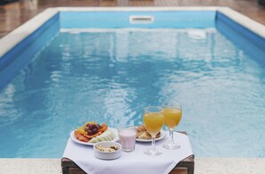 A poolside table with a plate of fruit, two glasses of orange juice, and a small bowl of nuts. - Cyan Americas Towers Hotel (Buenos Aires)