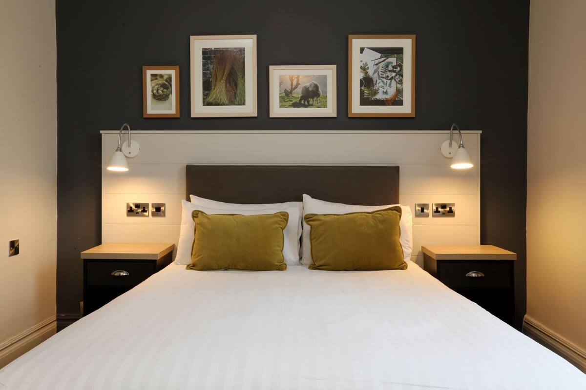 A neatly made bed with two pillows, a dark headboard, and framed pictures on the wall above.