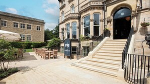 A historic building with a stone facade, a staircase leading to the entrance, outdoor seating area, and a sign for 'The Harrogate Inn'.