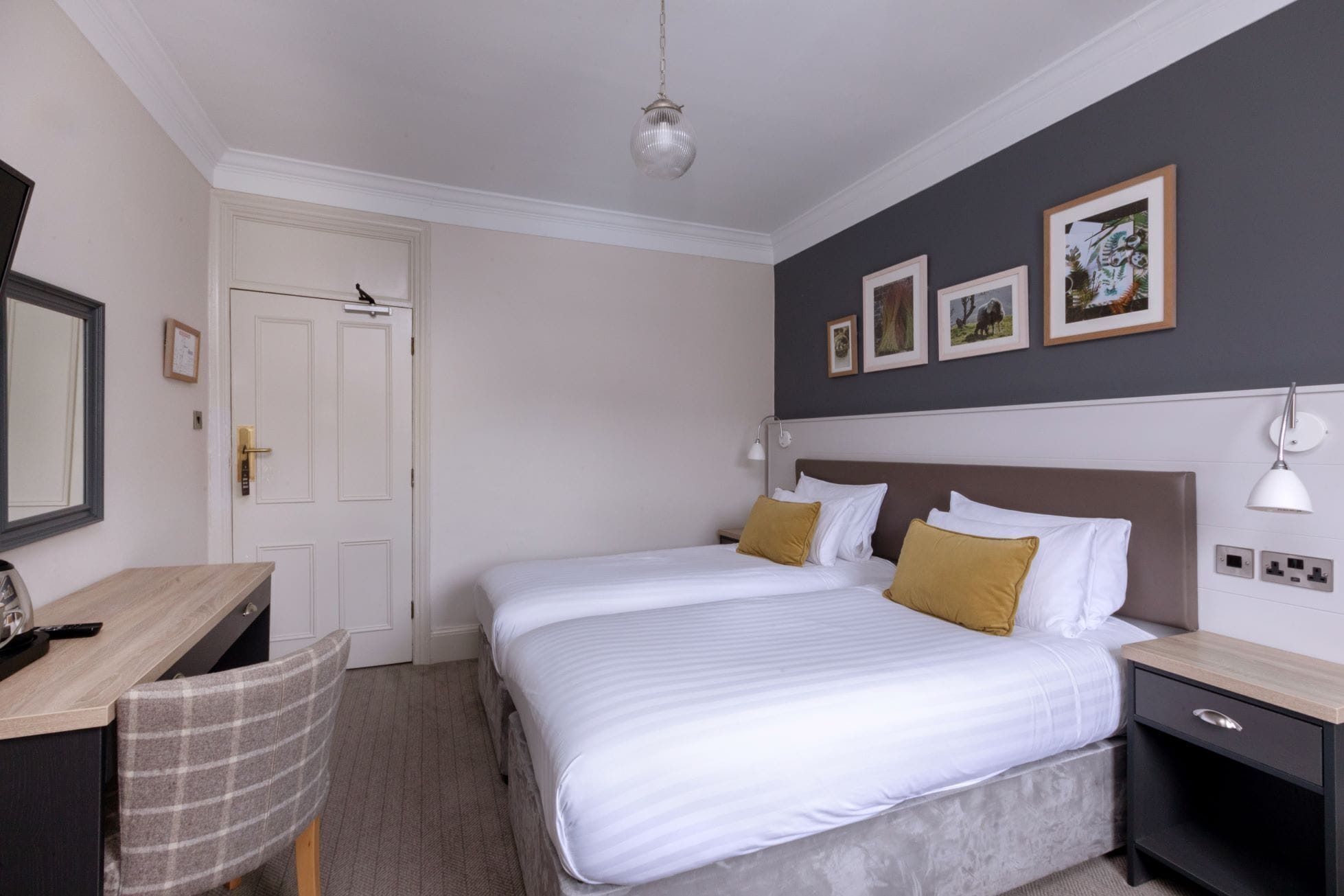 A hotel room with a bed, bedside tables, a desk, a chair, and a wardrobe.