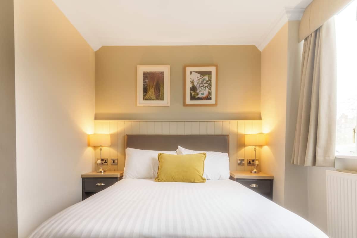 A hotel room with a large bed, two bedside lamps, a headboard, and two framed pictures on the wall.