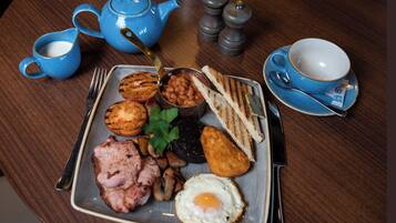 Une assiette de petit-déjeuner avec des œufs, du bacon, des toasts, des haricots et une théière, le tout posé sur une table en bois.