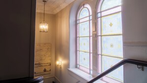 Una escalera con barandilla, un colgante de luz y una ventana con vidrios decorativos.