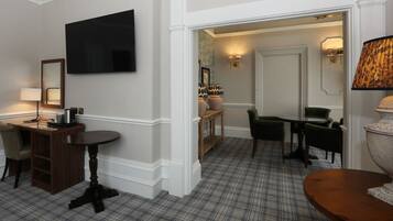A hotel room with a TV, a desk with a chair, a small table, a sofa, and a lamp.