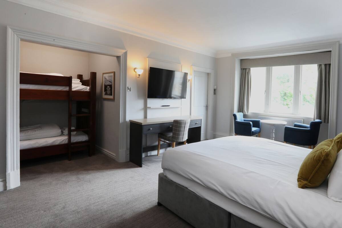 A hotel room with a bunk bed, a desk with a chair, a television, and a large window with curtains.