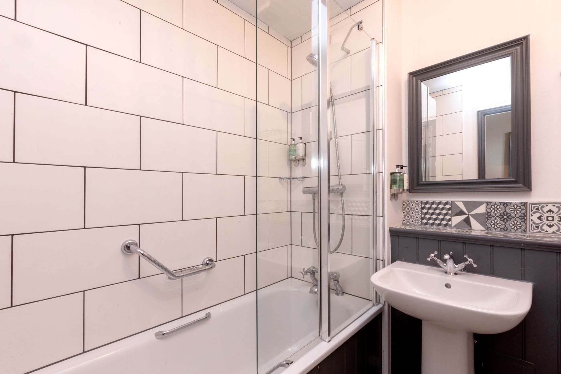 A bathroom with a glass-enclosed shower, a white sink, and a mirror above it.