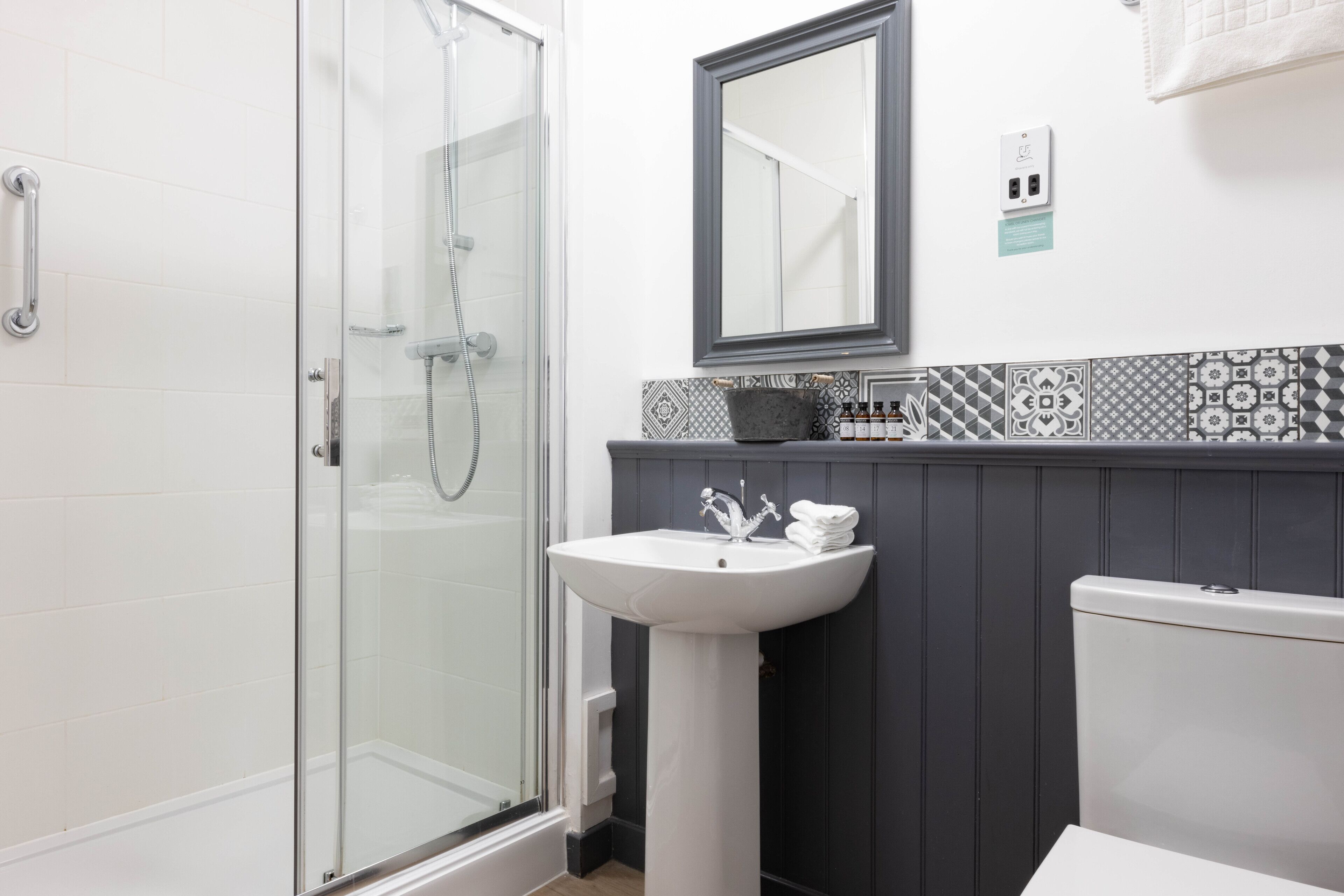 Un baño con cabina de ducha de vidrio, un lavabo blanco y un espejo sobre él.