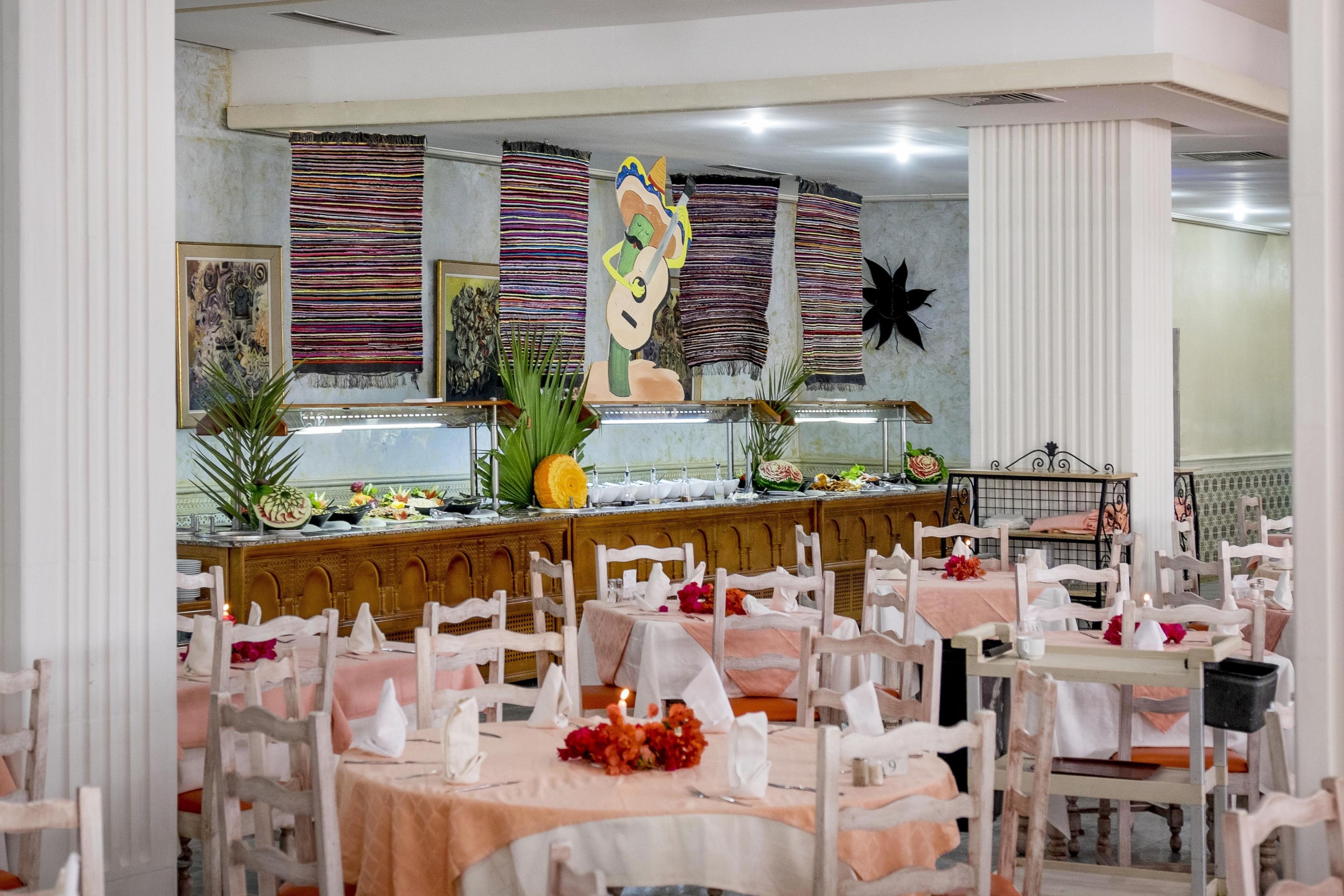 Um restaurante com várias mesas e cadeiras, um buffet com diversos pratos e decorações nas paredes.