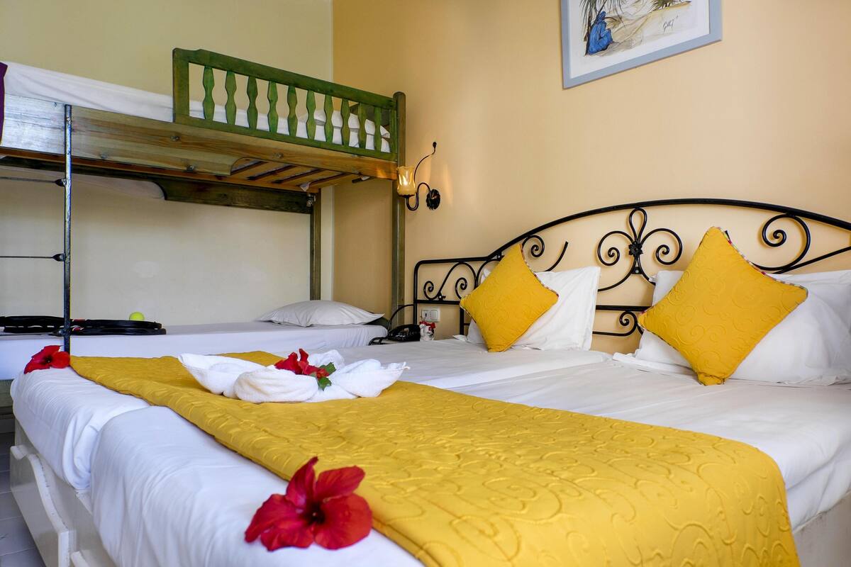A hotel room with two beds, one with a green headboard and the other with a black headboard. There are yellow pillows and a yellow blanket on one bed, and white bedding on the other.