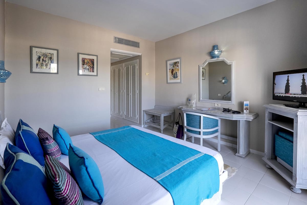 A hotel room with a bed, a desk, a television, and artwork on the walls.