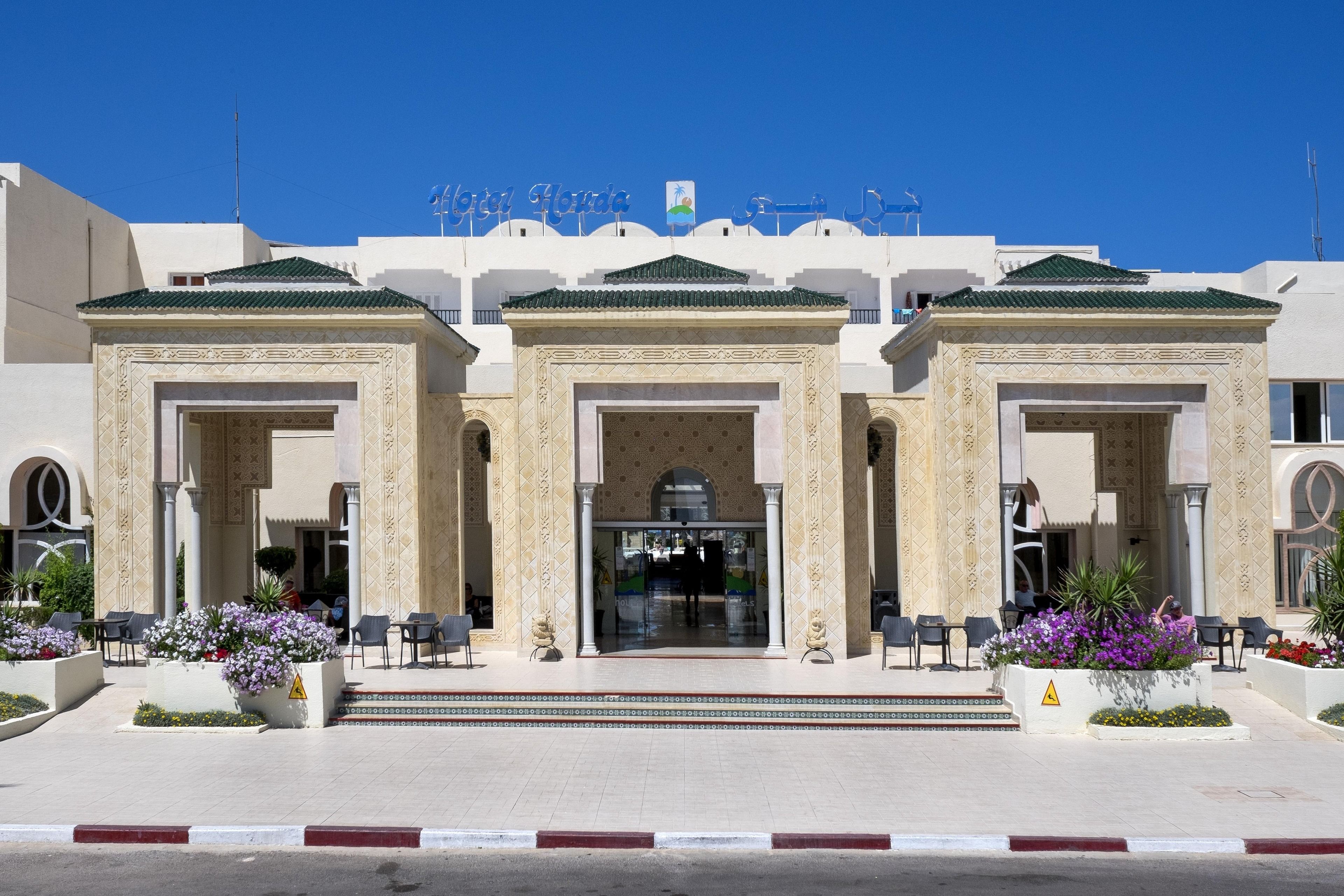 A hotel entrance with three arches, a sign above reading "Alma Honda", and a tiled pathway leading to the entrance.