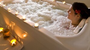 Una bañera llena de burbujas, rodeada de velas encendidas, con una persona relajándose en ella.