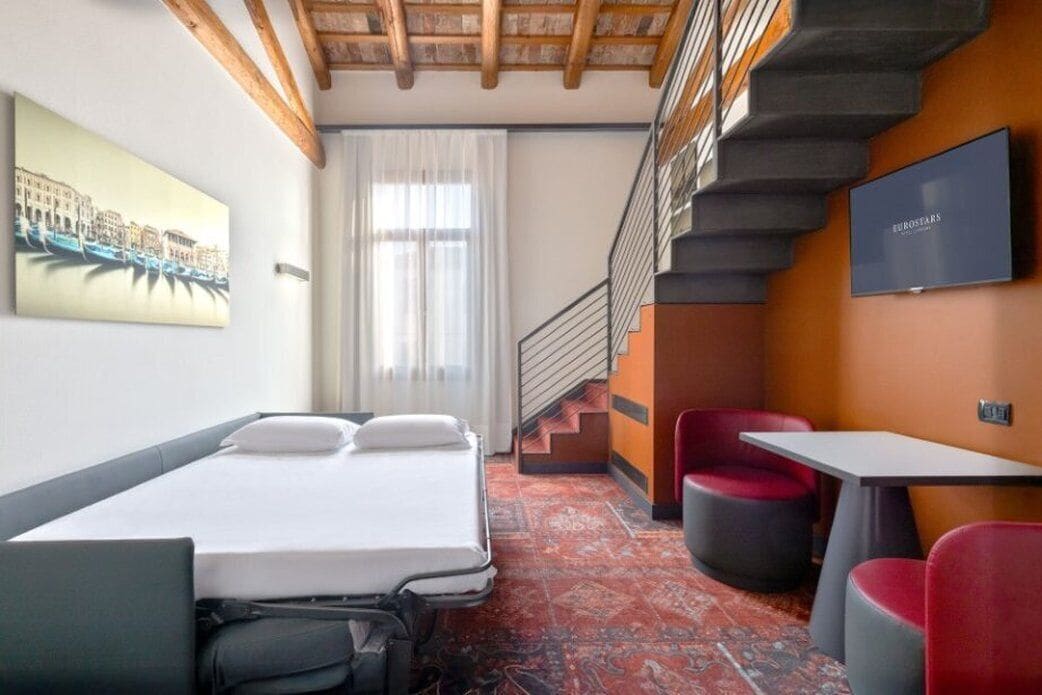 Une chambre d’hôtel avec un lit, un bureau, une chaise, une télévision et un escalier.
