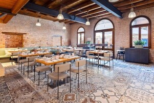 Un restaurante con paredes de ladrillo, vigas de madera y suelo de baldosas estampadas. Mesas y sillas dispuestas para comer.
