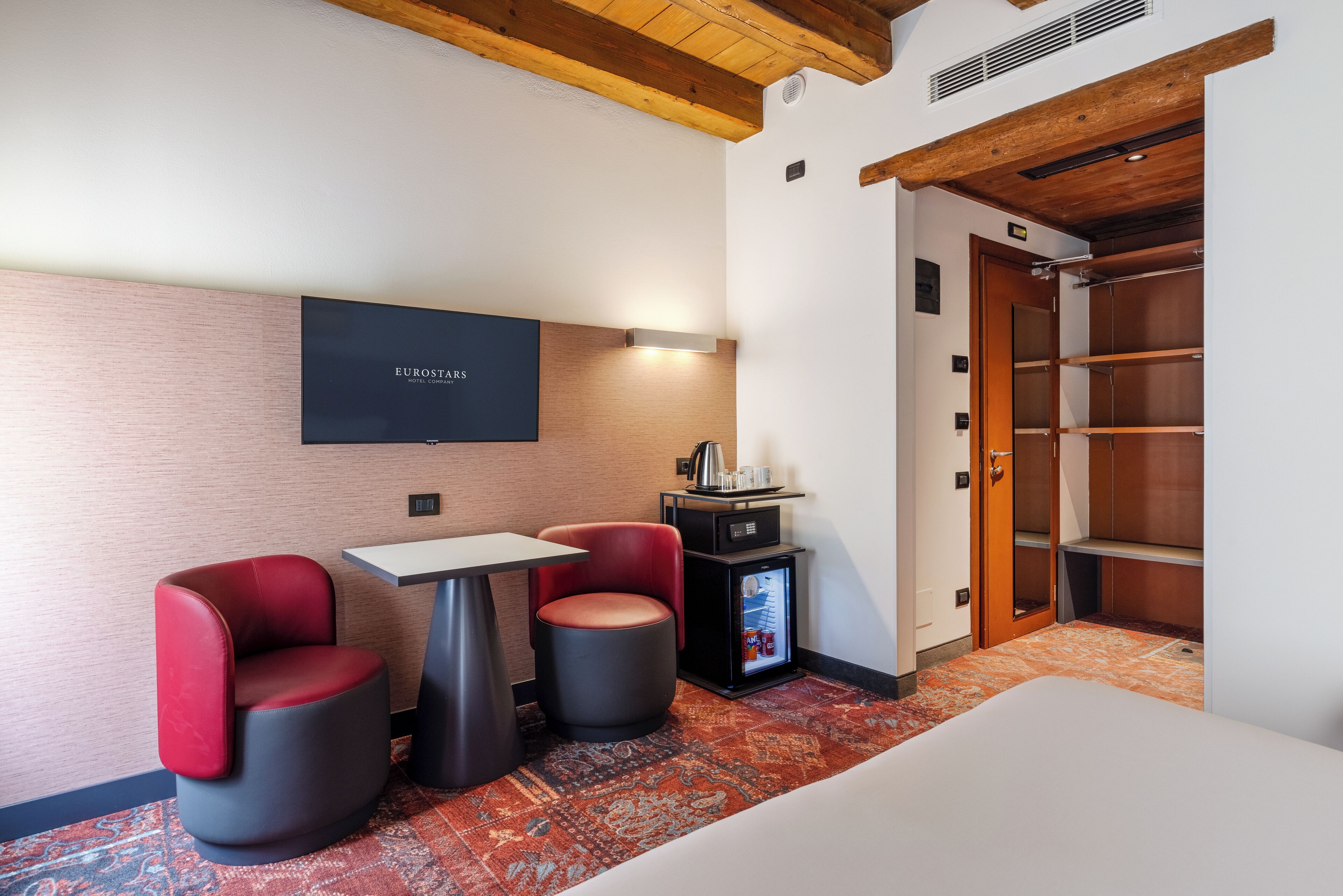 Habitación de hotel con cama, dos sillones, una mesita, minibar y televisión en la pared.