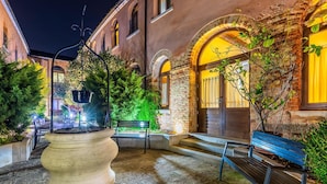 An outdoor courtyard with a large planter, benches, and a building with arched windows. - Eurostars Cannaregio (Venice)