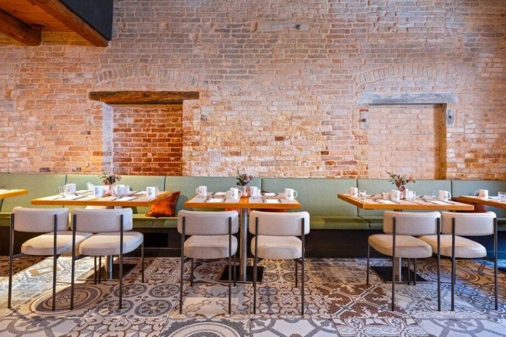 A restaurant with brick walls, green cushioned seating, and patterned floor tiles.